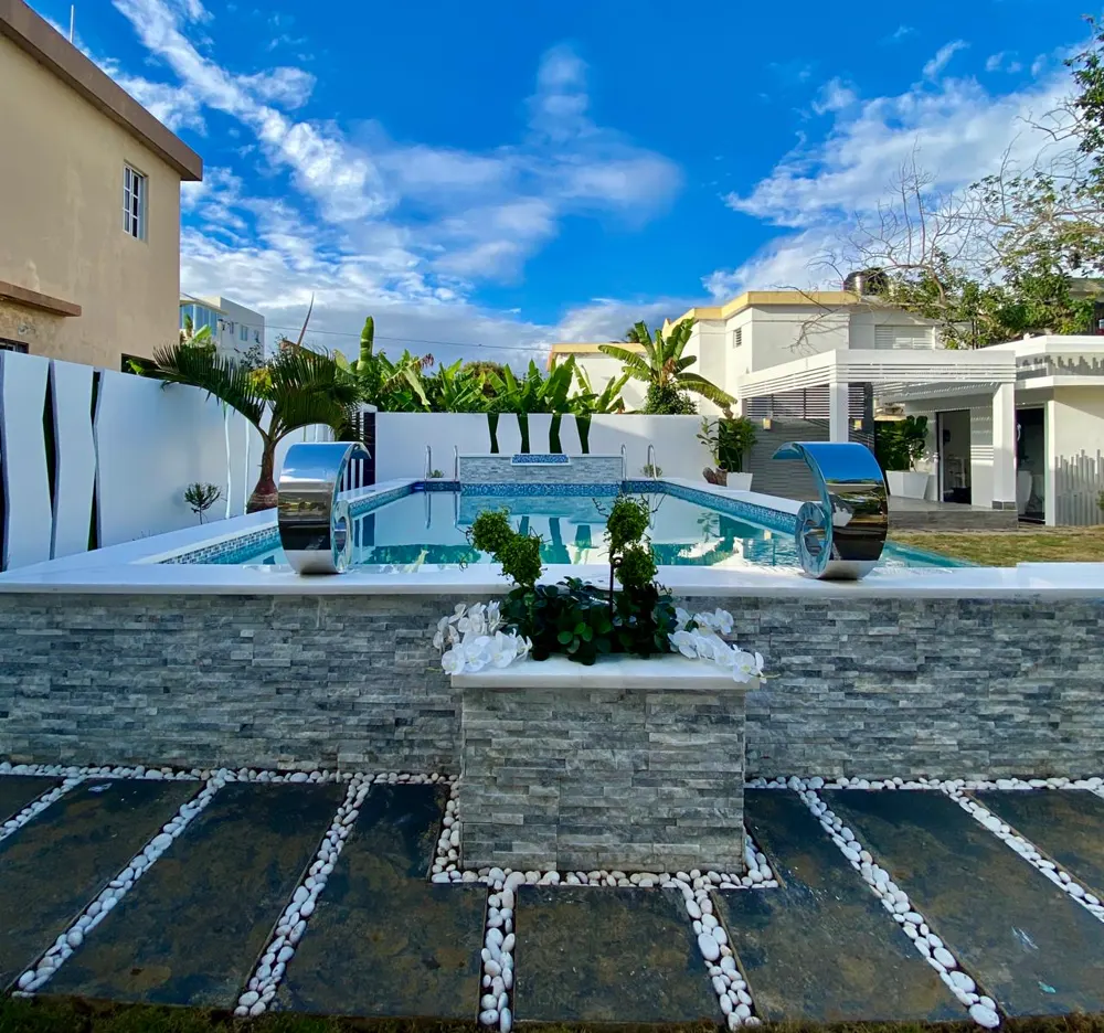 Piscina elevada con muro de piedra y esculturas de agua cromadas